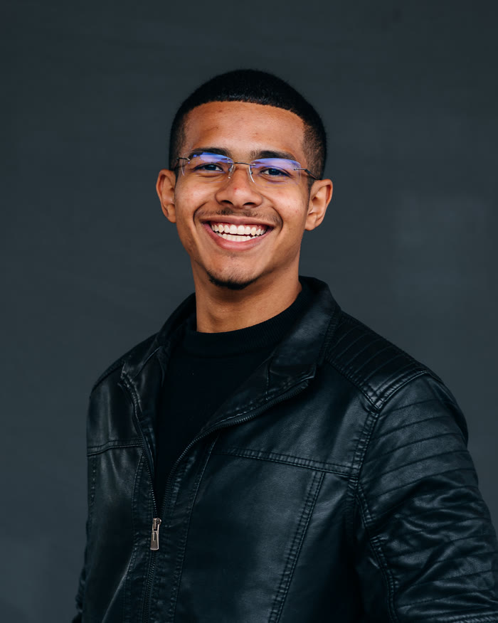 Lucas Evangelista sorrindo, de jaqueta de couro, no estúdio